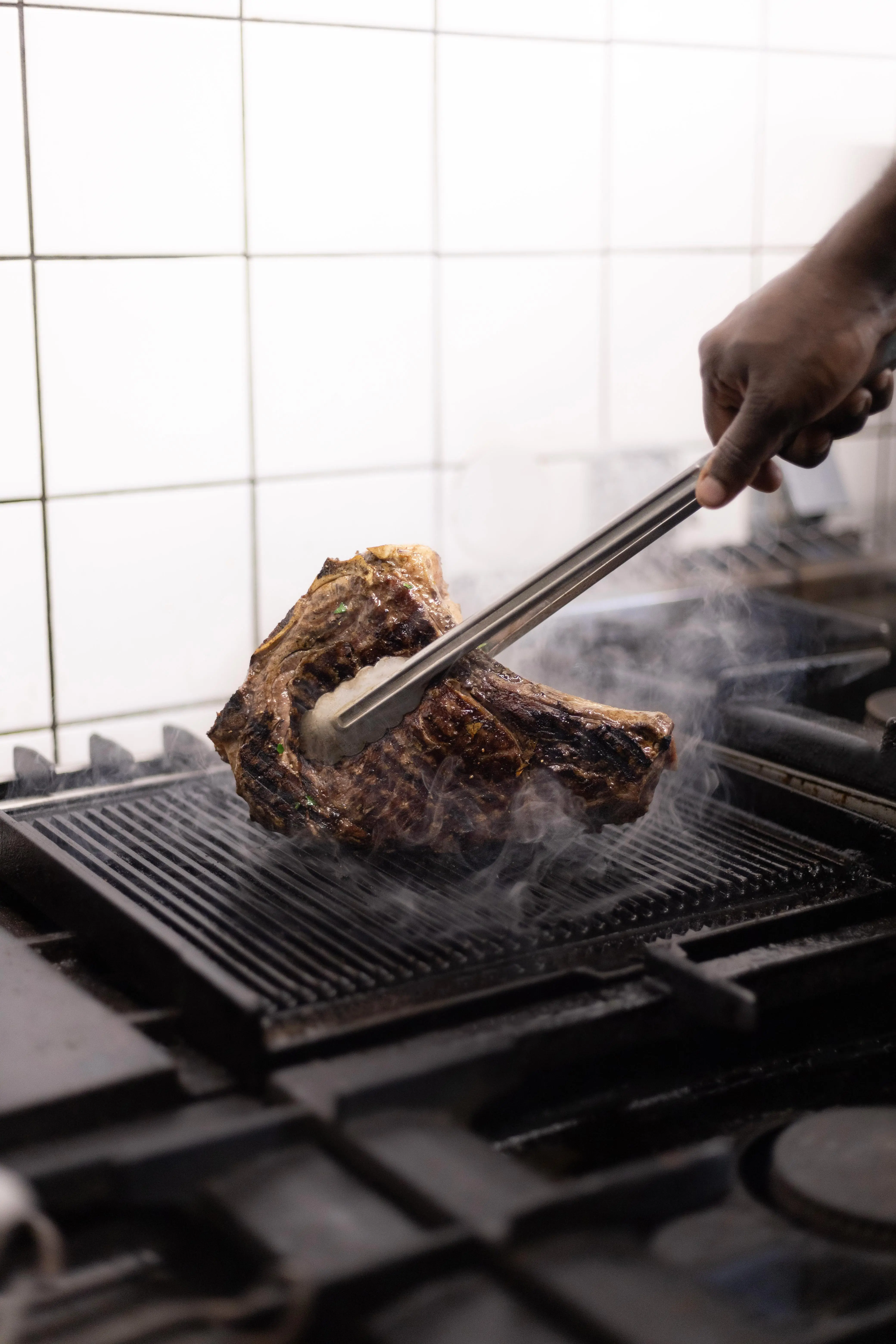 The chef grills a cut of meat with tongs
